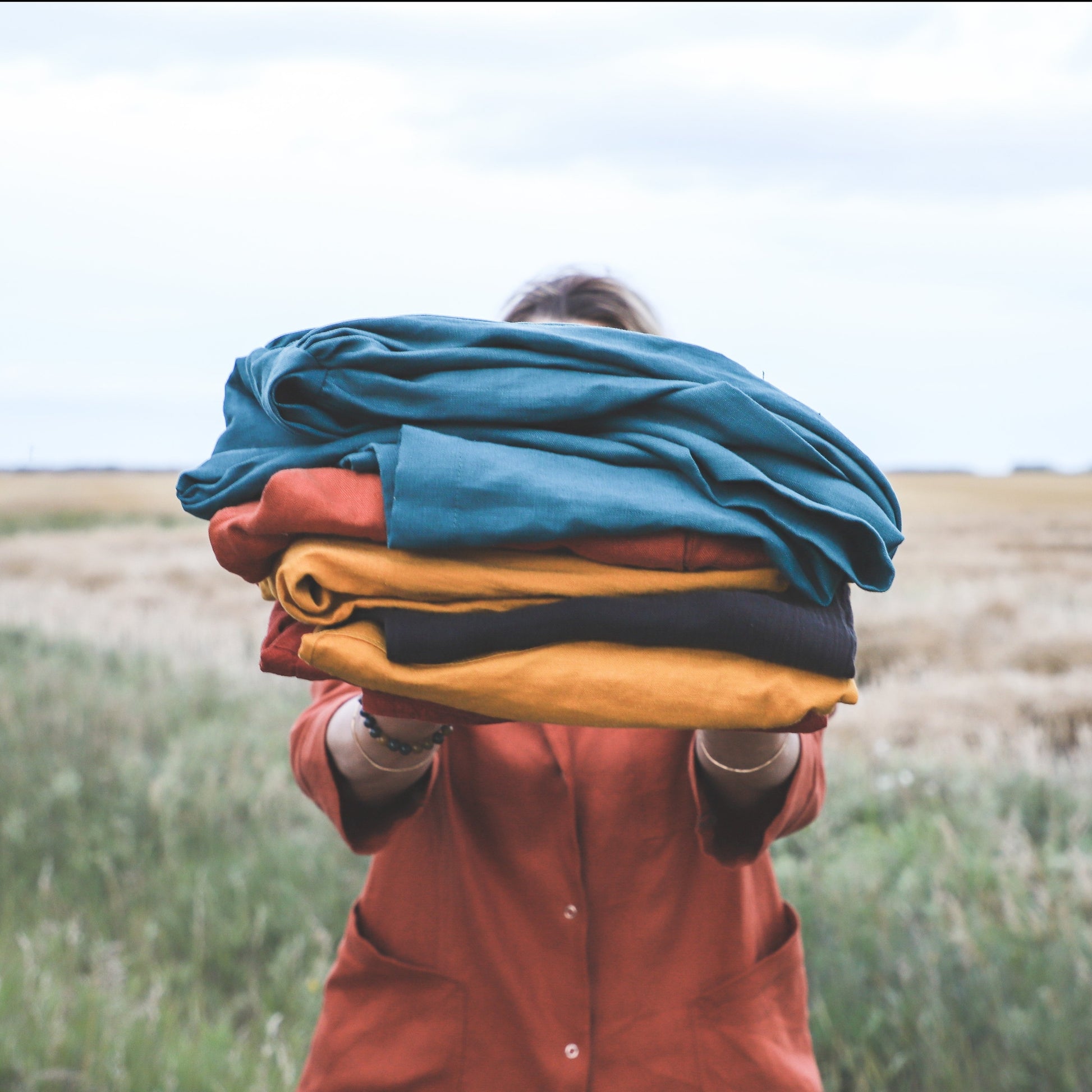 model holding in front of her a pile of folded linen clothes standing in a field
